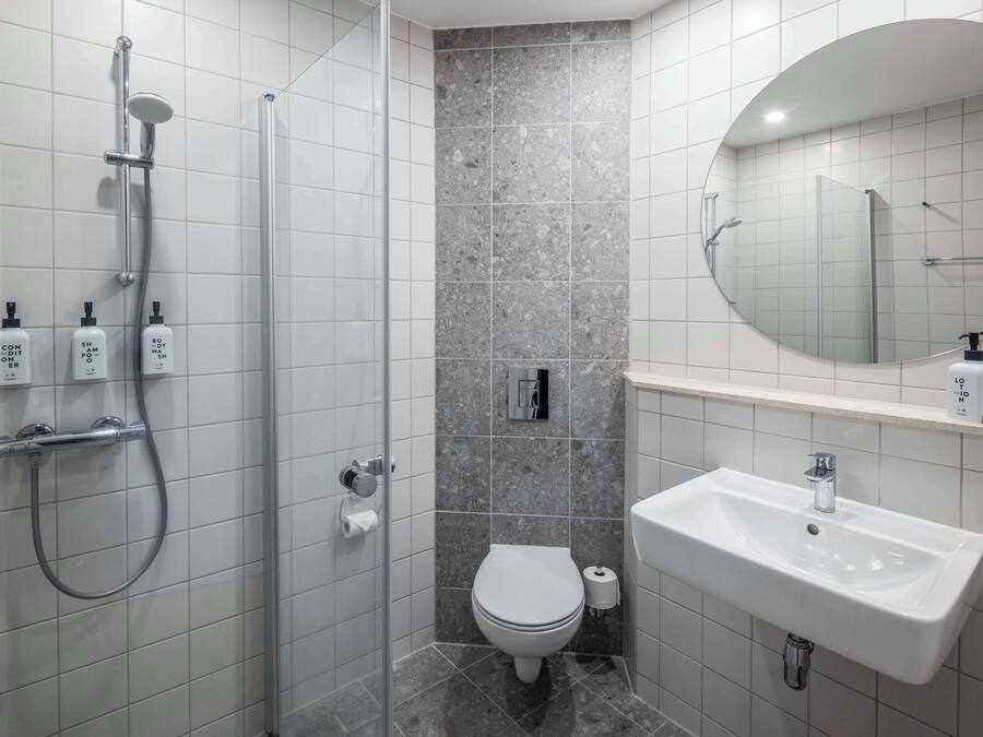 A modern bathroom with a shower, toilet, sink, and a mirror.