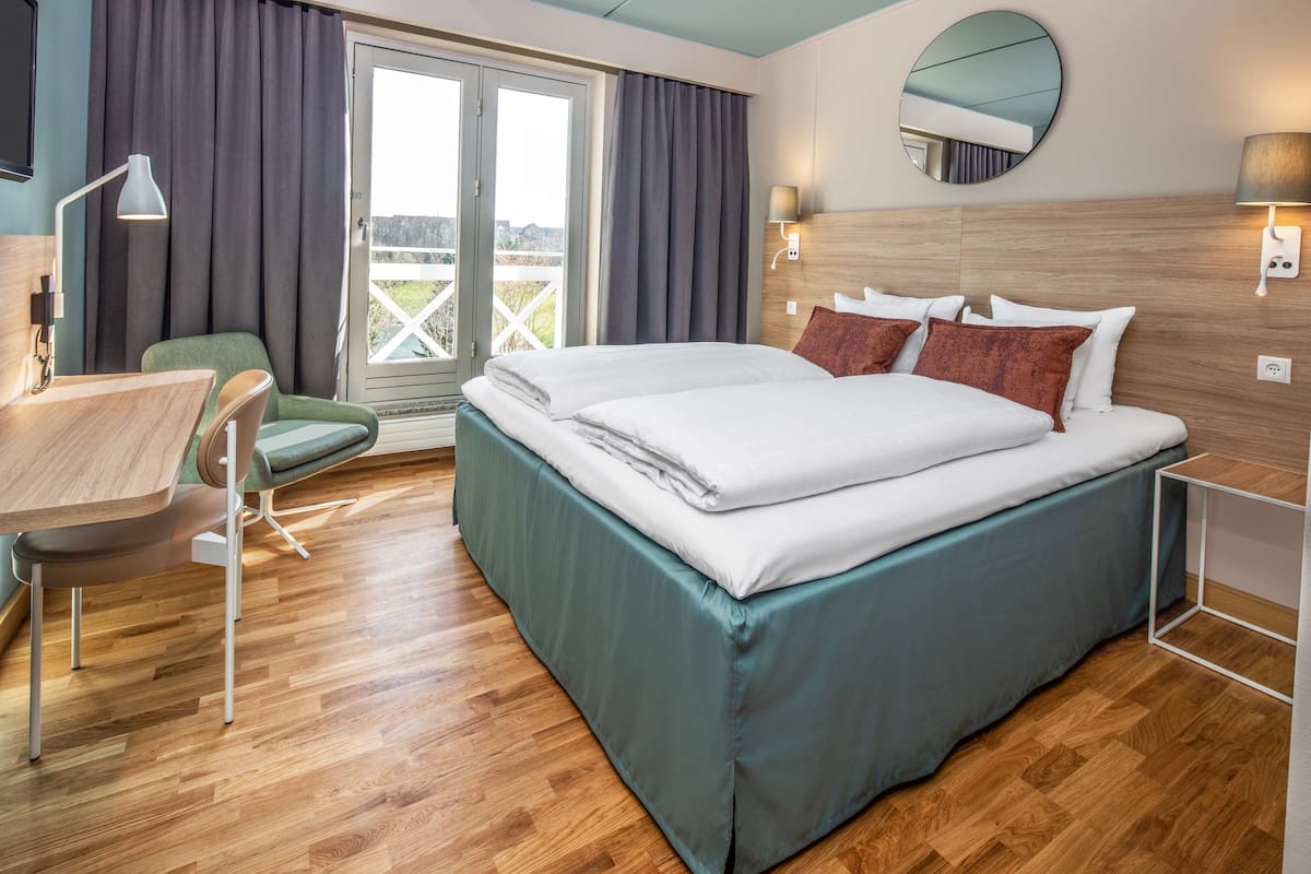 Quarto de hotel com cama, escrivaninha, cadeira e vista para o exterior por uma porta de correr.