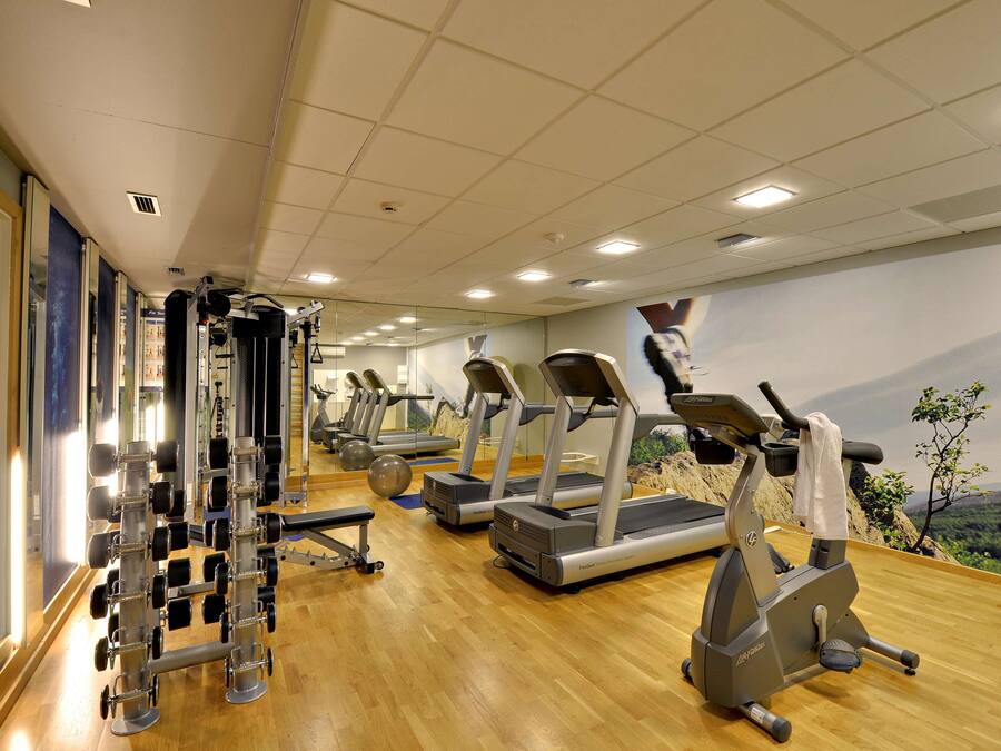 Een sportschool met loopbanden, krachtapparaten en een houten vloer.