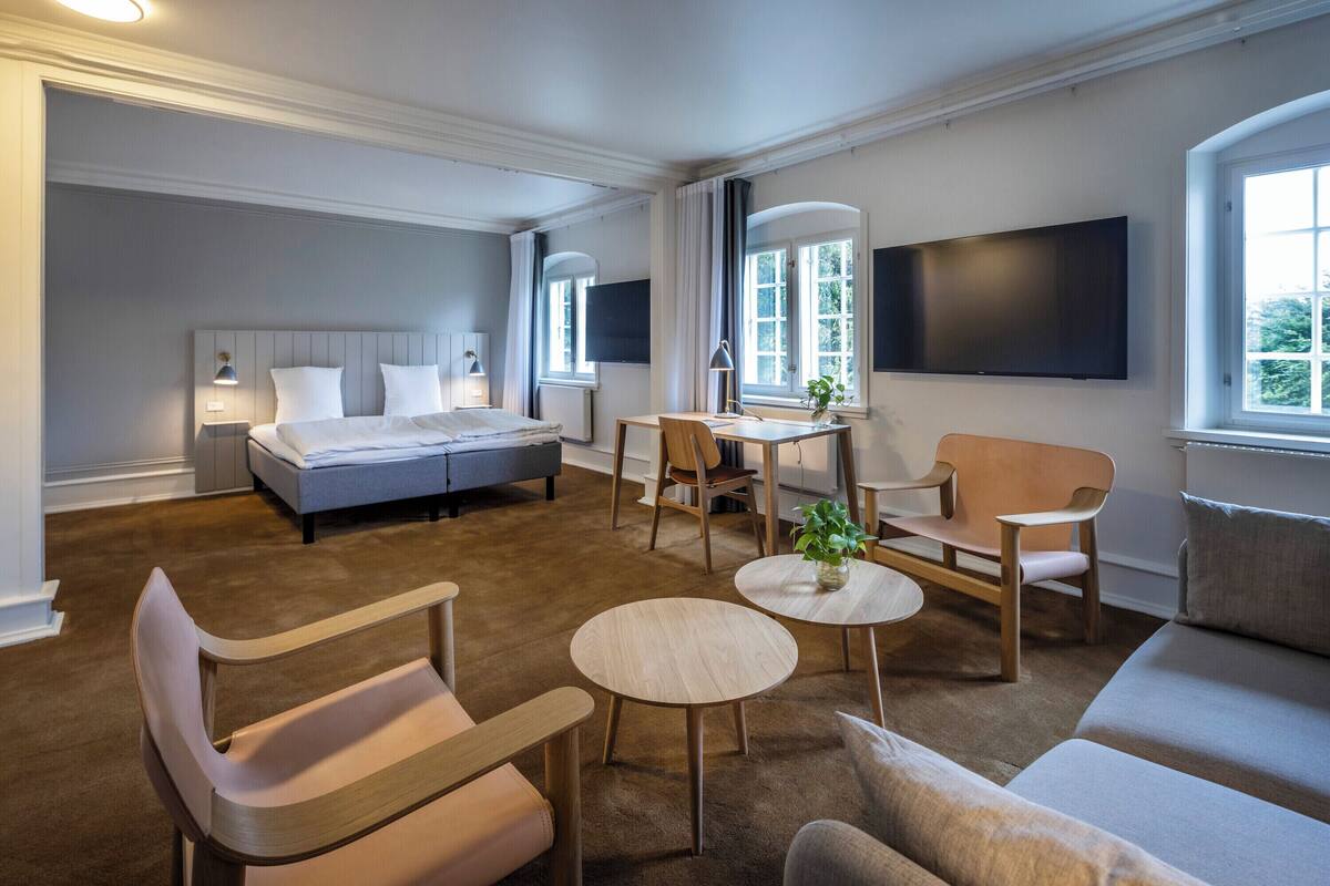 A hotel room with a bed, a desk, two chairs, a sofa, and a TV mounted on the wall.