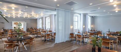 Un comedor amplio con varias mesas y sillas, ventanas grandes e iluminación en el techo.