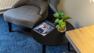 A room with a grey armchair, a small round table with a magazine, and a potted plant.