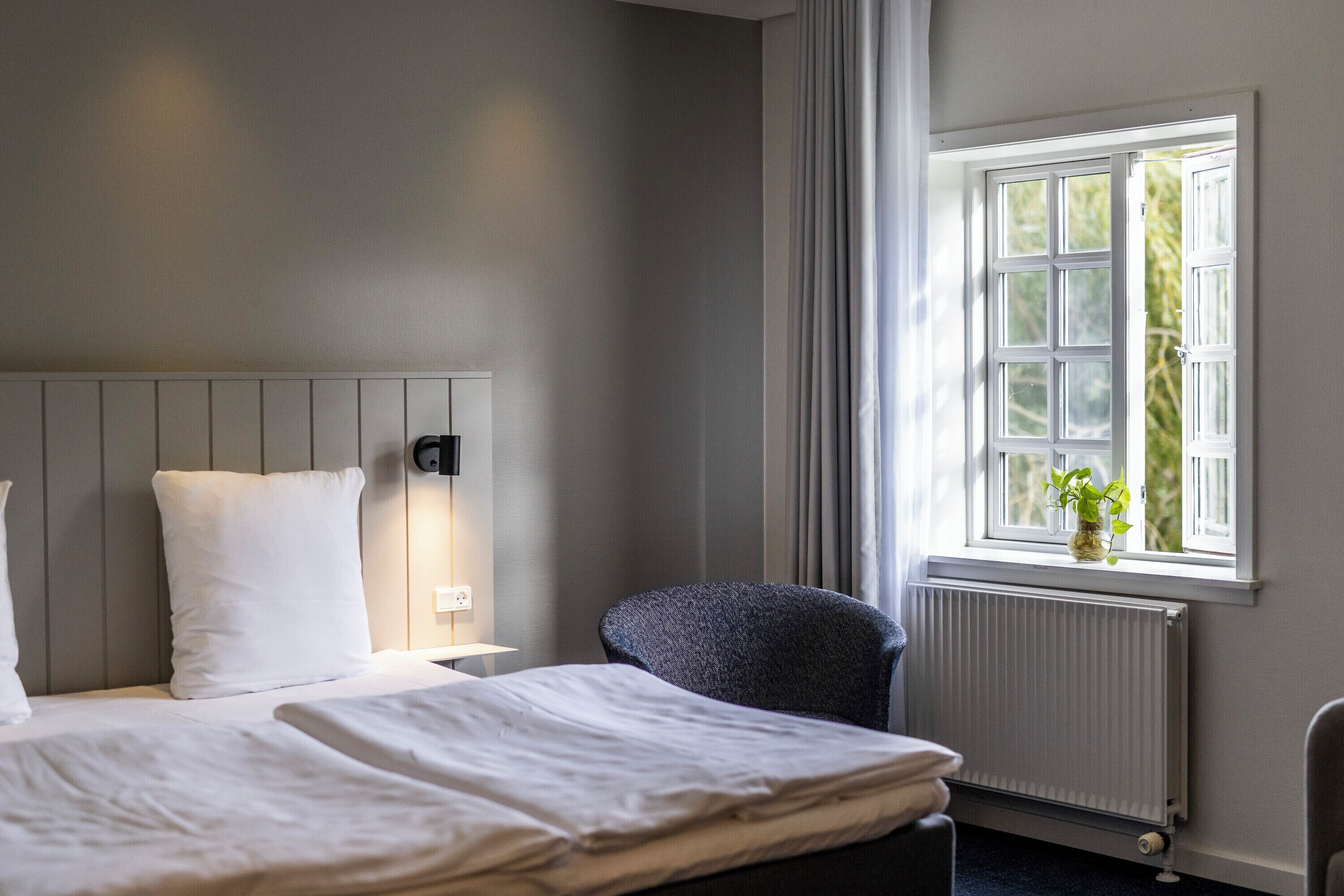Una habitación de hotel con cama, una silla, una ventana con cortinas y un radiador.