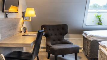 Een hotelkamer met een houten bureau, een zwarte fauteuil, een nachtkastje, een lamp en een raam met uitzicht op groen.