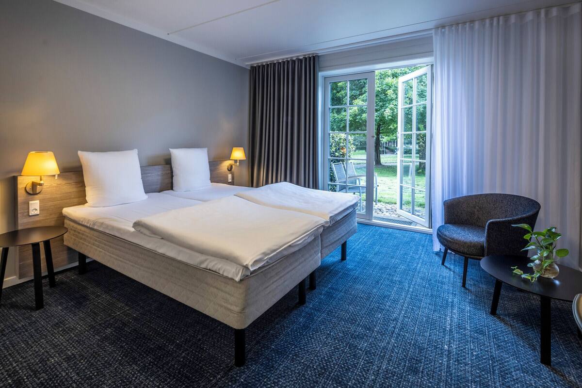 A hotel room with a large bed, two bedside tables with lamps, a chair, and a view of the outdoors.