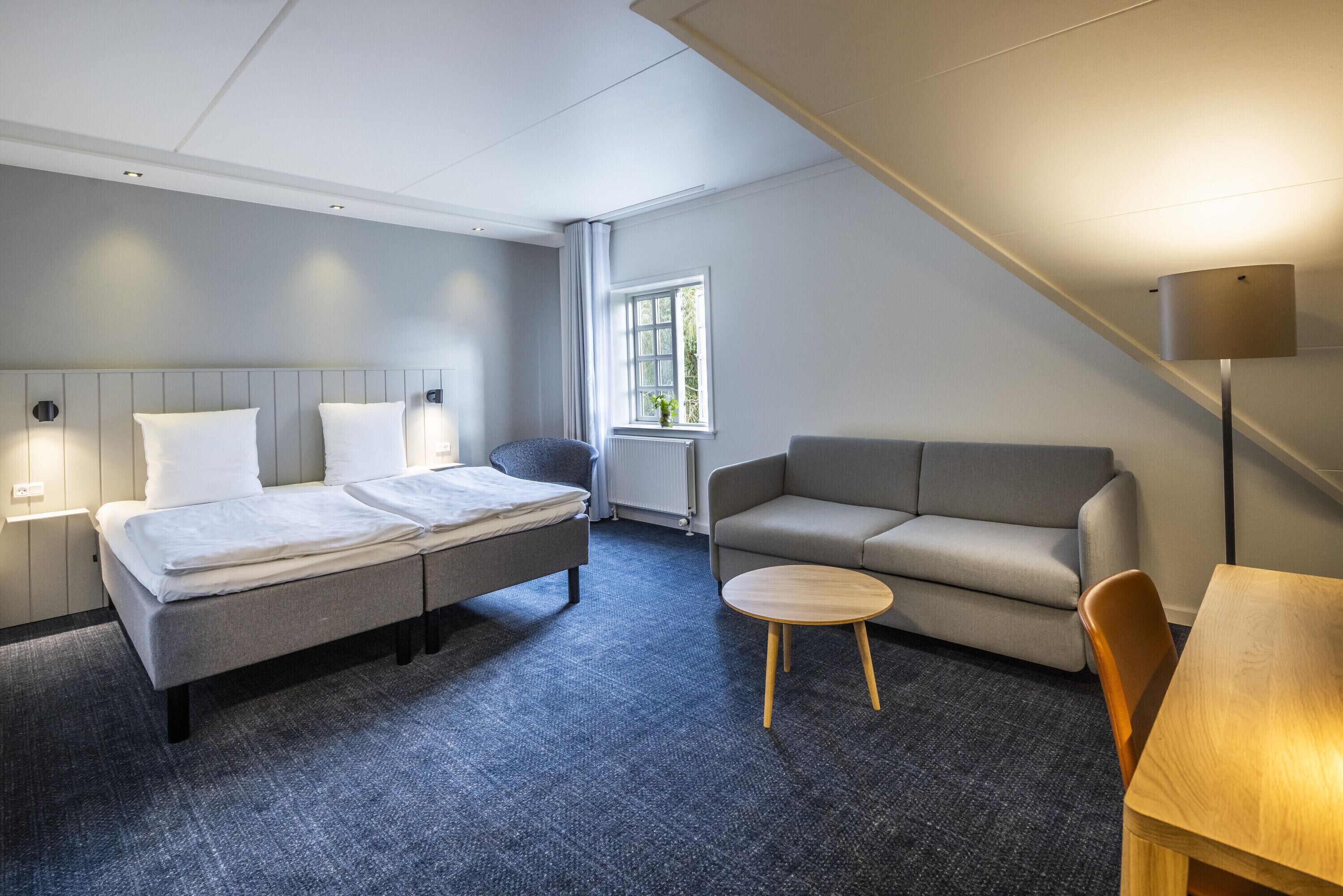 A hotel room with a bed, a sofa, a small table, and a lamp.