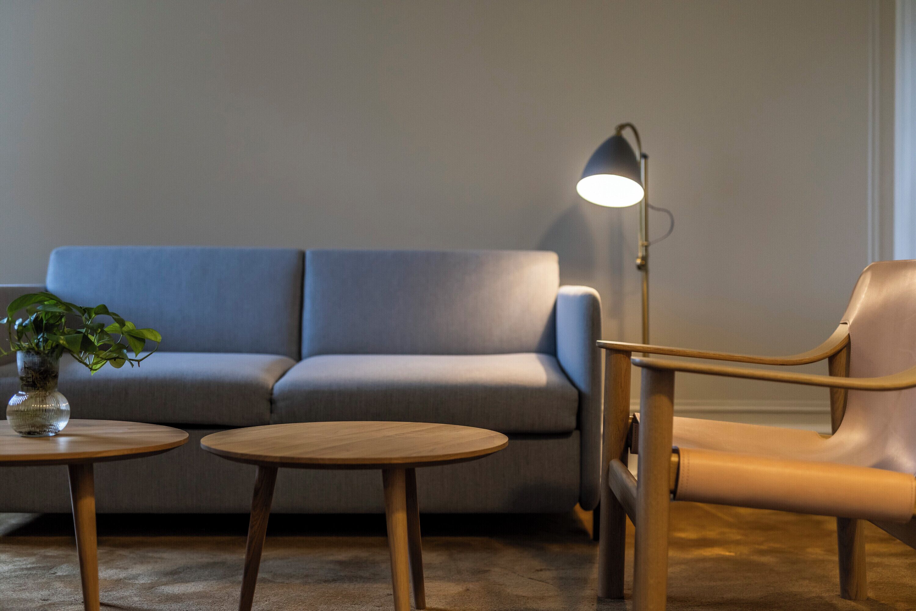 En moderne stue med en grå sofa, to træsideborde, en læderlænestol og en gulvlampe.