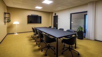 A conference room with a long table, six chairs, a white floor lamp, a television on the wall, and a door with a frosted glass panel.