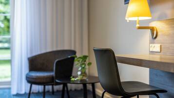 Habitación de hotel con escritorio, dos sillas, lámpara y una pequeña mesa con una planta.