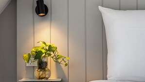 A bedroom with a bed, a bedside table with a plant, a wall-mounted light, and a white pillow. - Comwell Bygholm Park (Horsens)