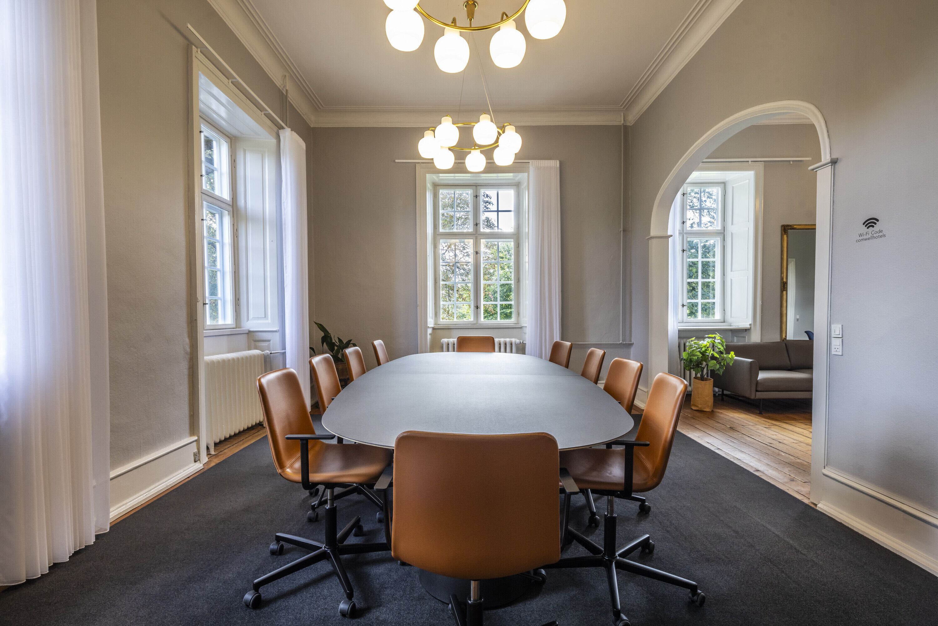 A conference room with a large oval table, leather chairs, and a chandelier.