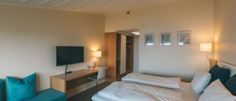Una habitación de hotel con una cama, un escritorio con televisor, una silla y un sofá.