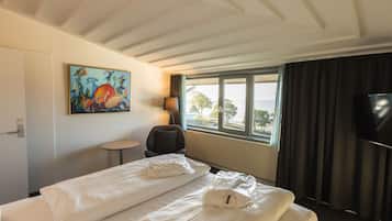 Una habitación de hotel con cama, una silla, televisión, un cuadro y ventana con vista.
