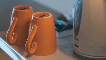 Dos tazas anaranjadas sobre una bandeja, junto a una tetera eléctrica blanca.