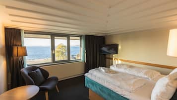 Ein Hotelzimmer mit Bett, Sessel, Fernseher und einem Fenster mit Meerblick.