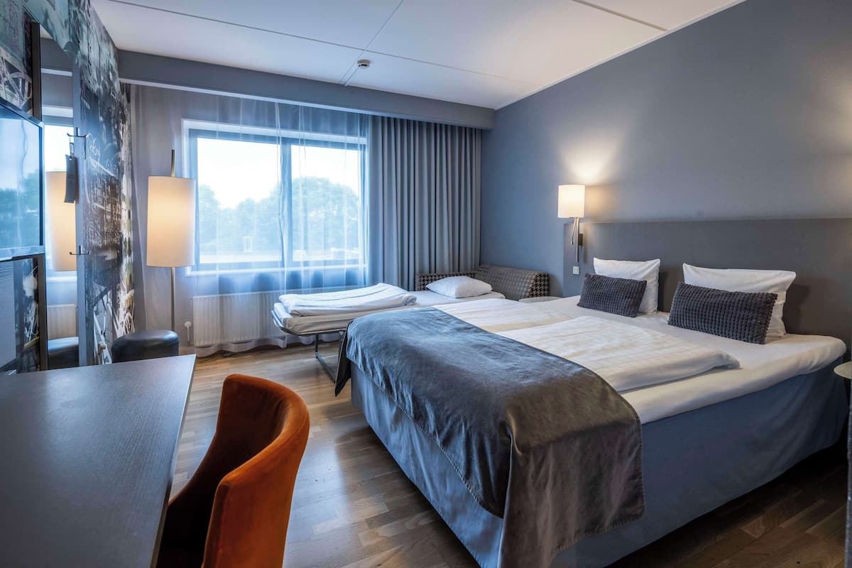 A hotel room with a large bed, a desk, and a chair.