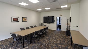 A conference room with a long table, chairs, a flat-screen TV, framed artwork, and a clock on the wall.