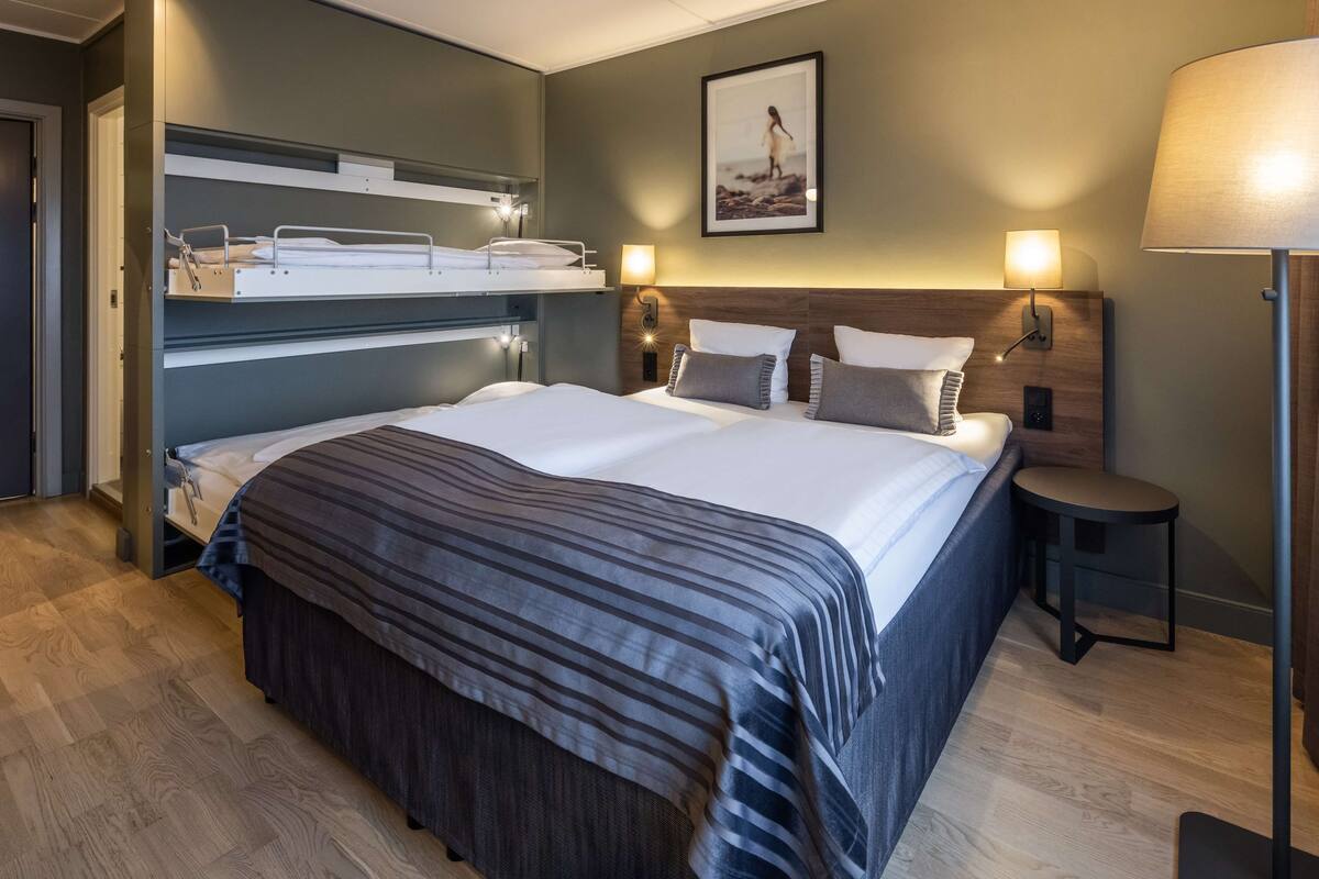 A modern hotel room with a large bed, a bedside table, a lamp, and a picture on the wall.