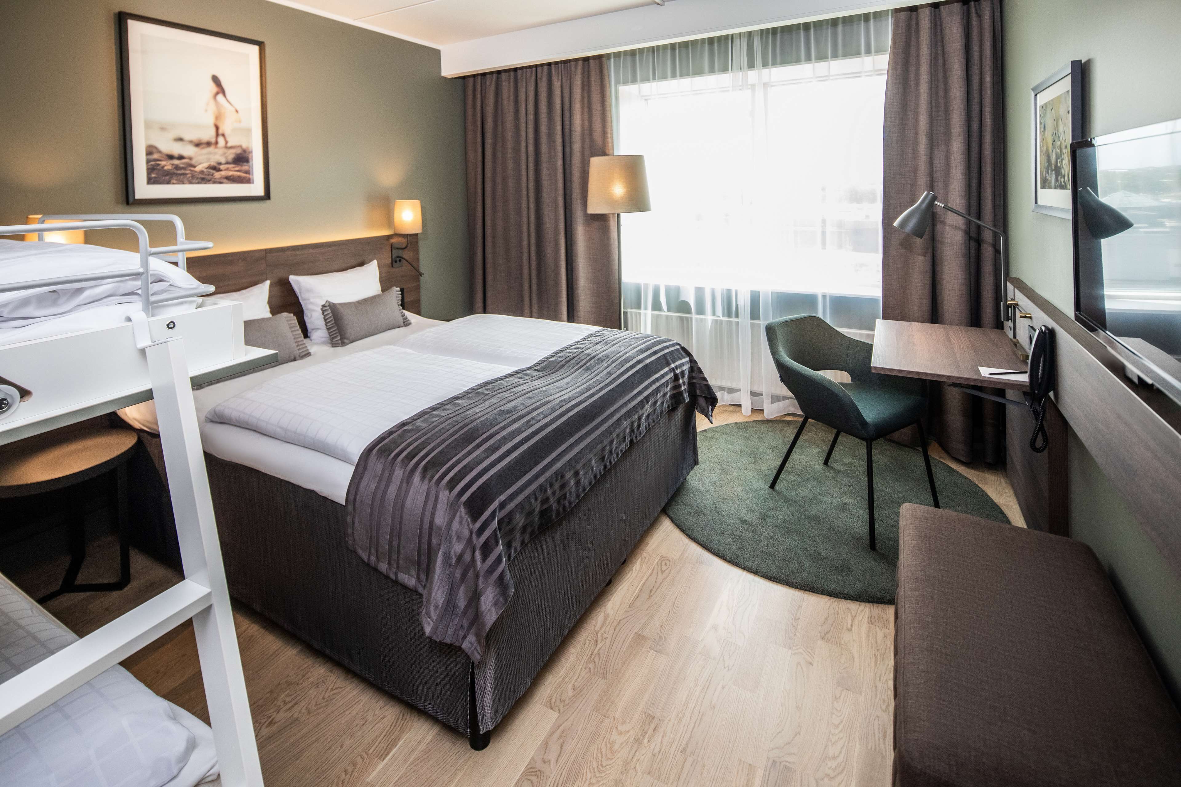 Habitación de hotel con cama, escritorio, silla y vistas al exterior.
