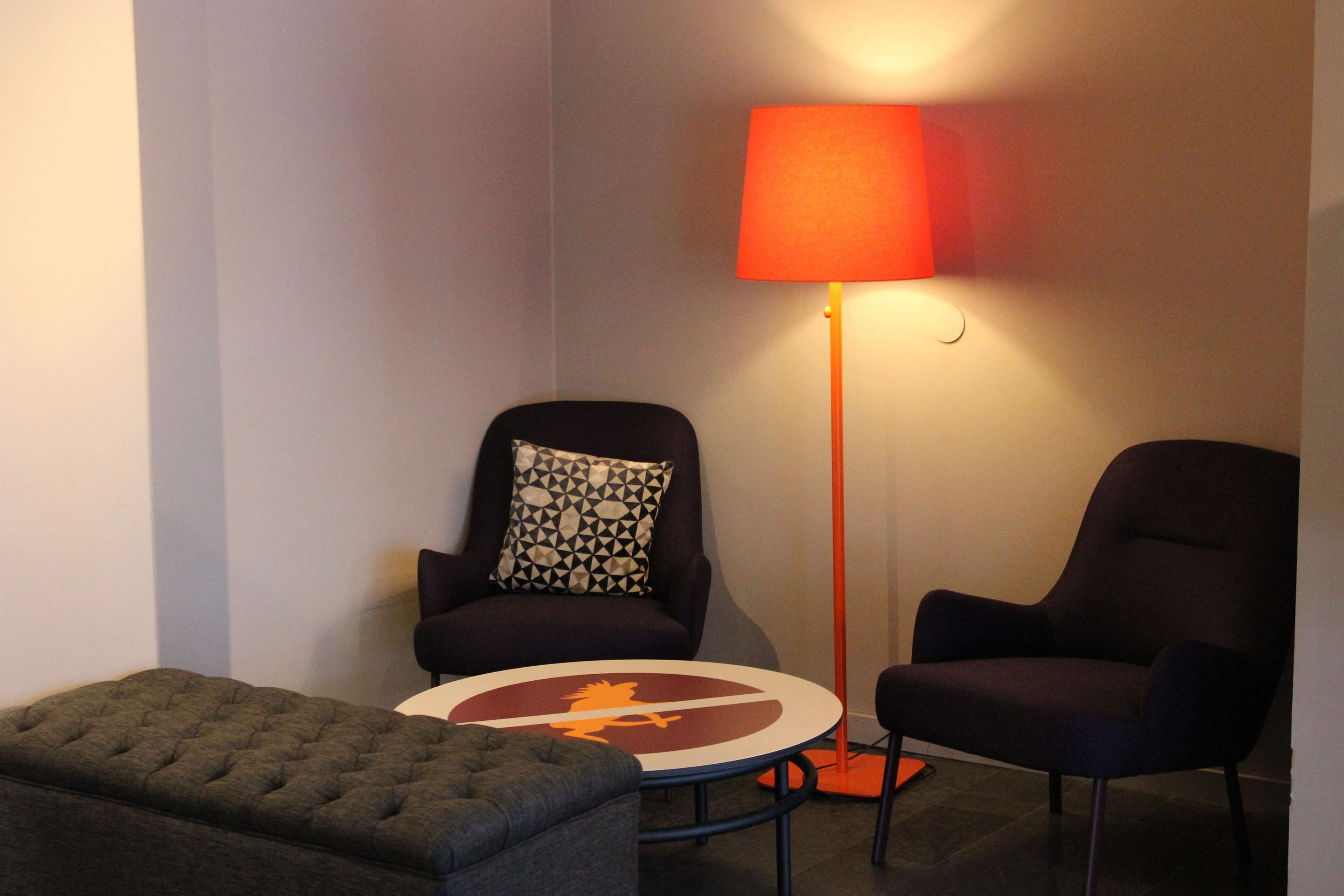 A room with a round table, two armchairs, a floor lamp, and a tufted ottoman.