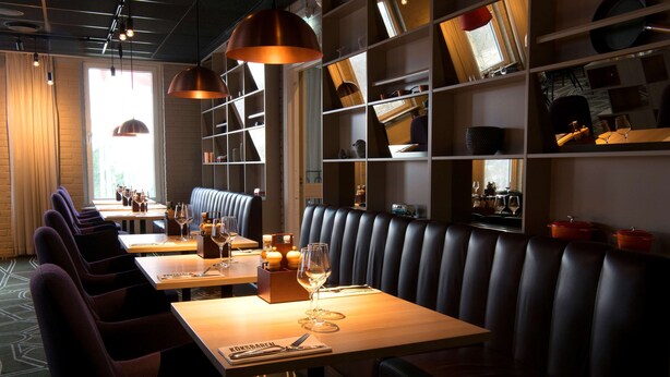 Un restaurant avec des banquettes et des tables, un plancher en bois et des luminaires suspendus.