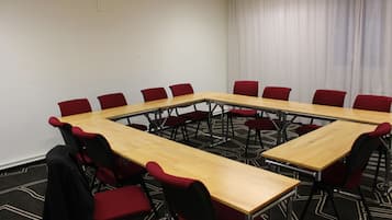Ett konferensrum med ett långt bord och röda stolar, heltäckningsmatta på golvet och ett fönster med gardiner.