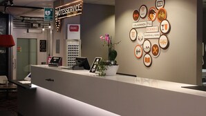 Un comptoir d’accueil avec une enseigne indiquant « MOTESSERVICE » et « AED » pour les services d’urgence. Différents pictogrammes sont affichés sur le mur pour indiquer les équipements et les services disponibles.