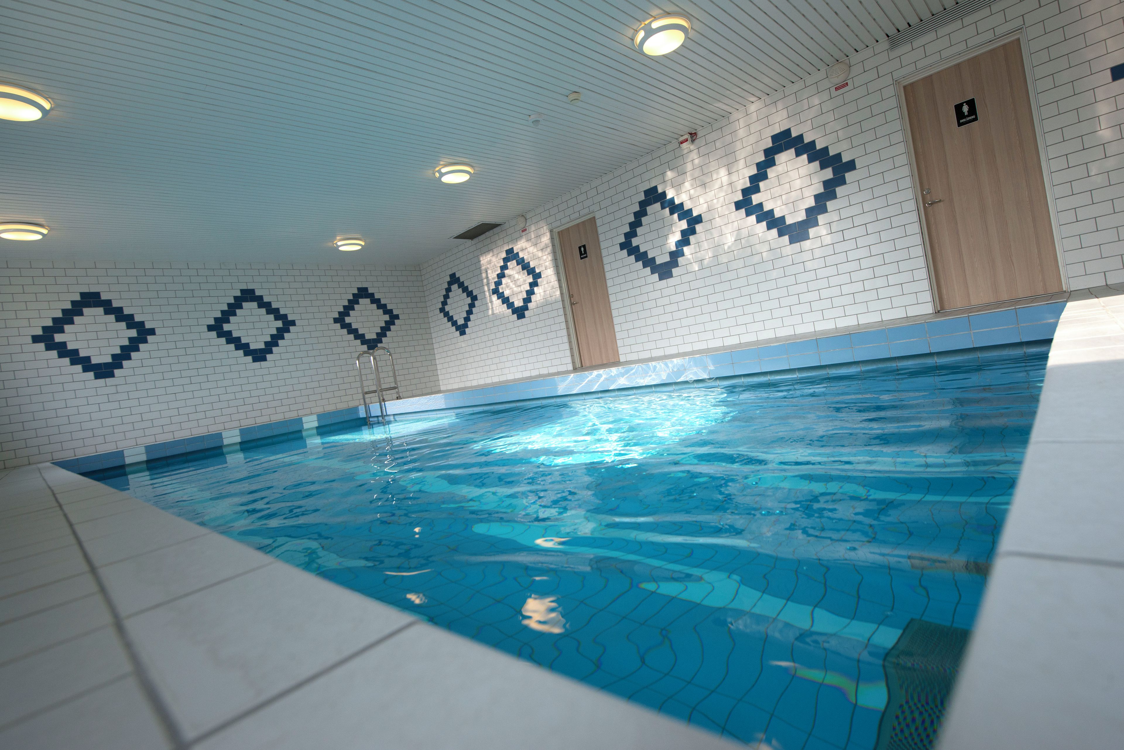An indoor swimming pool with tiled walls and ceiling, a wooden door, and a tiled floor.