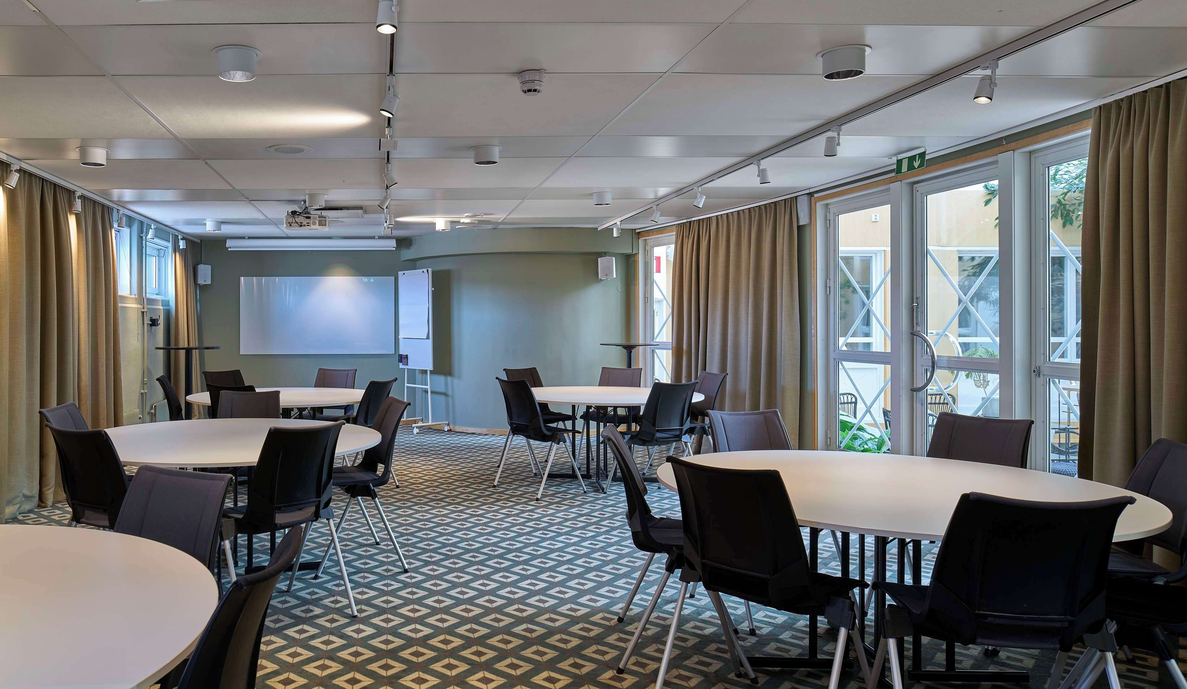 A conference room with tables and chairs, a projector screen, and a large window with curtains.