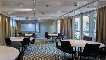 A conference room with tables and chairs, a projector screen, and a large window with curtains.