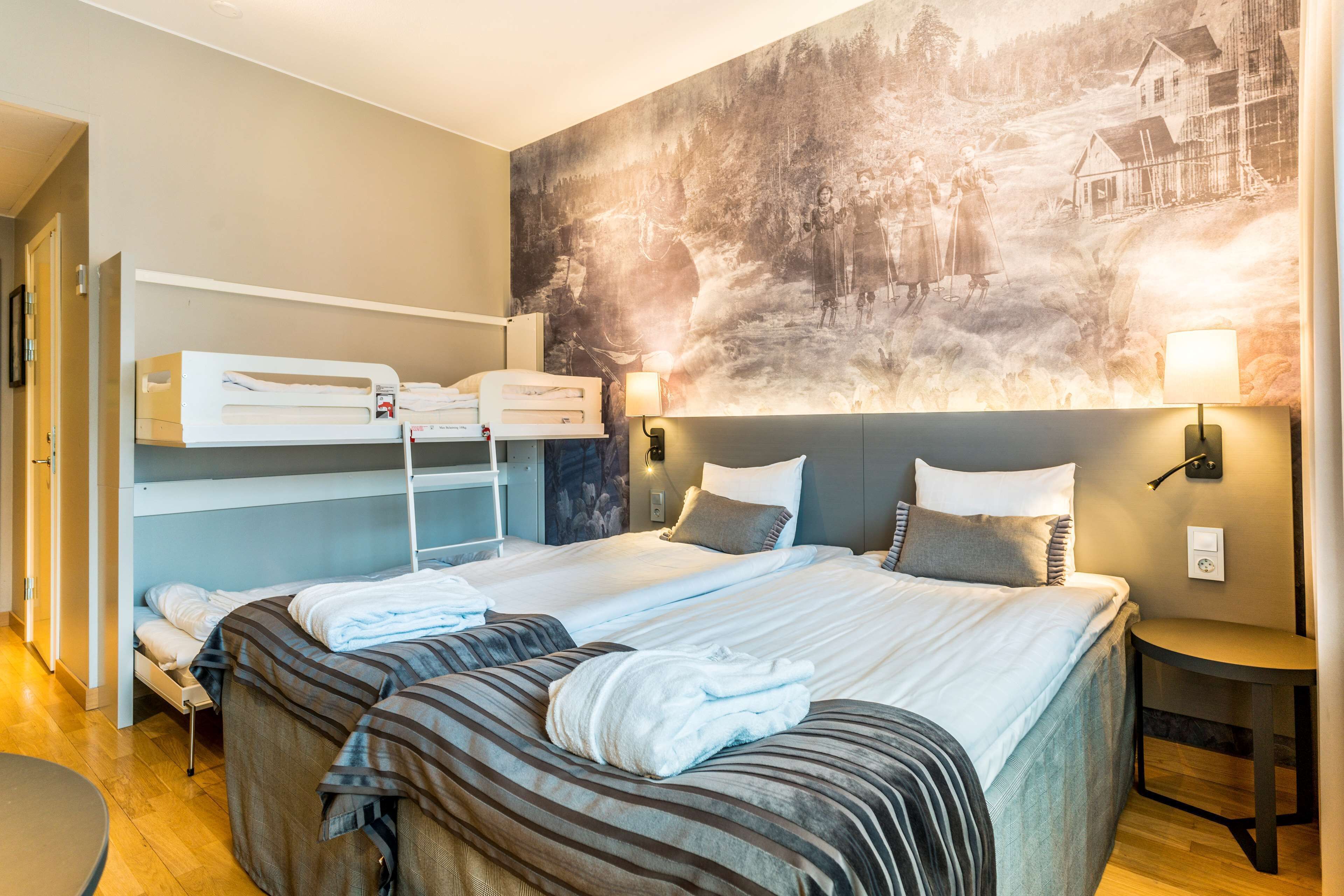 A hotel room with bunk beds, a large painting on the wall, and a small table with a lamp.