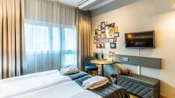 Ett hotellrum med två sängar, ett skrivbord, en stol, en tv och en vägg som är dekorerad med tavlor.