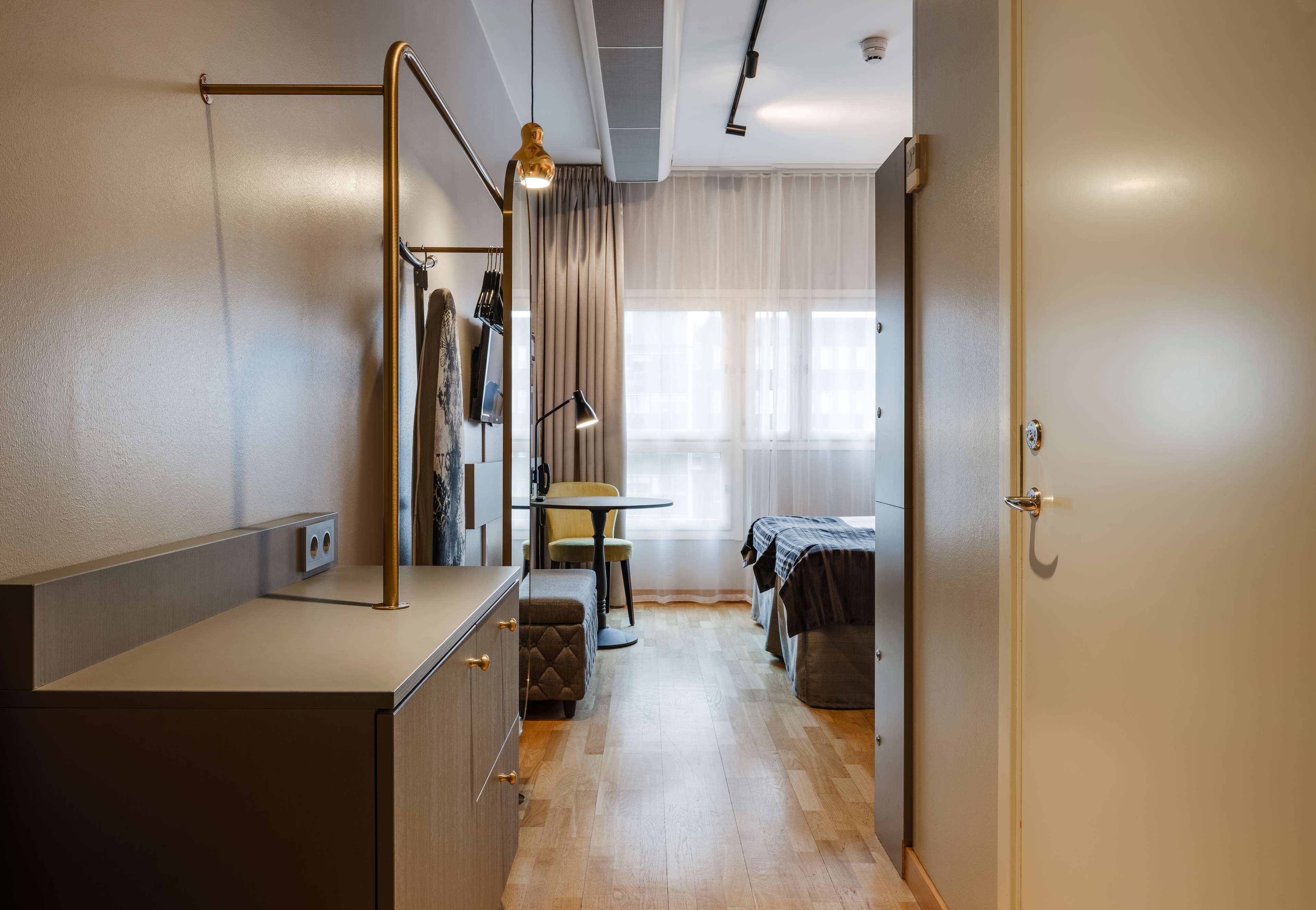 Une chambre d’hôtel de taille réduite, équipée d’une kitchenette, d’un lit, d’une petite table et d’une chaise.