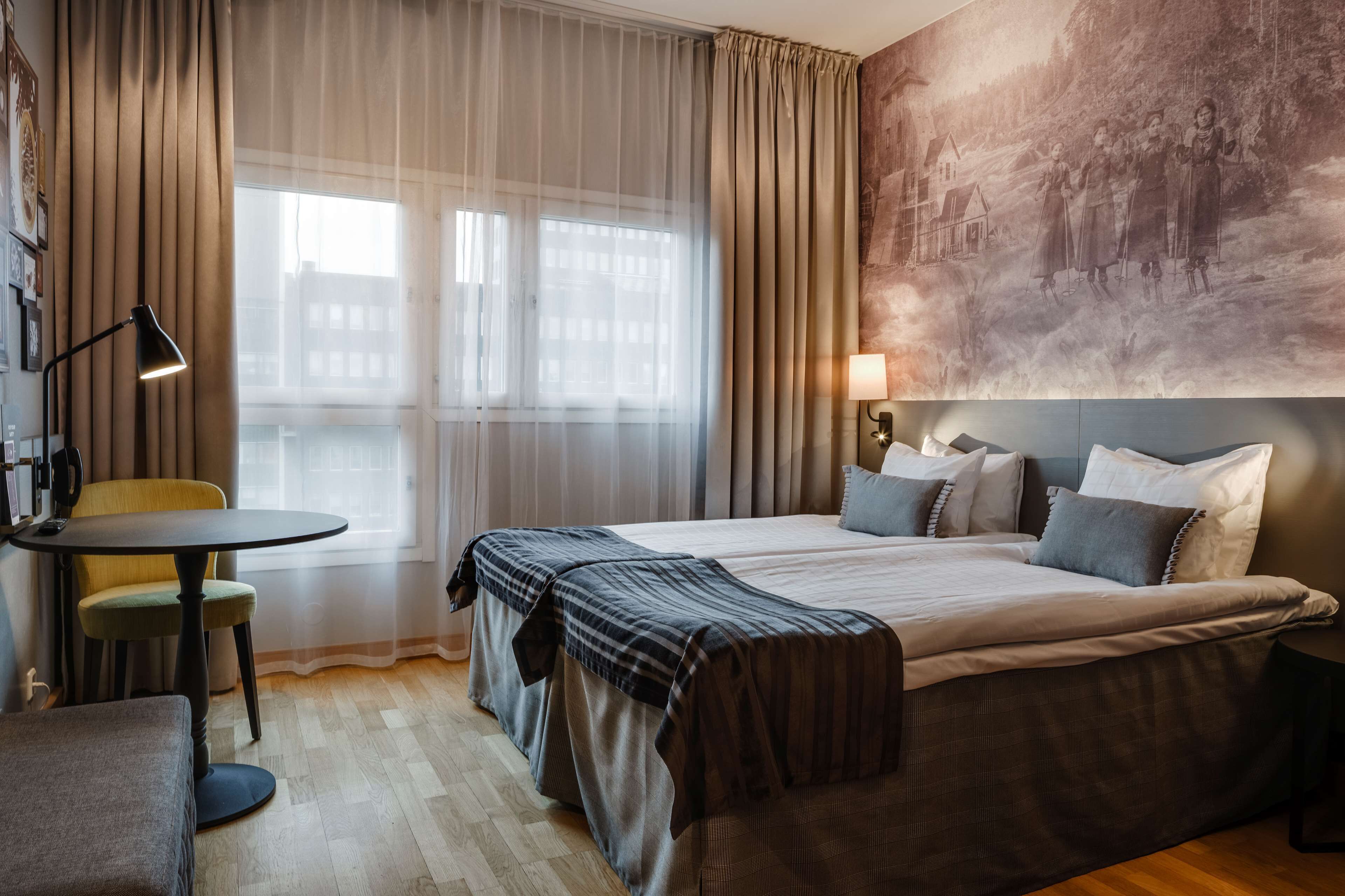 Une chambre d’hôtel avec un grand lit, une petite table avec une chaise, une lampe et un tableau au mur.