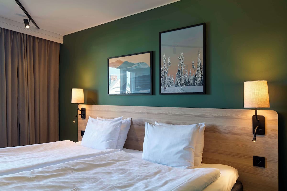 A hotel room with a large bed, two wall-mounted lamps, and two framed pictures on the wall.