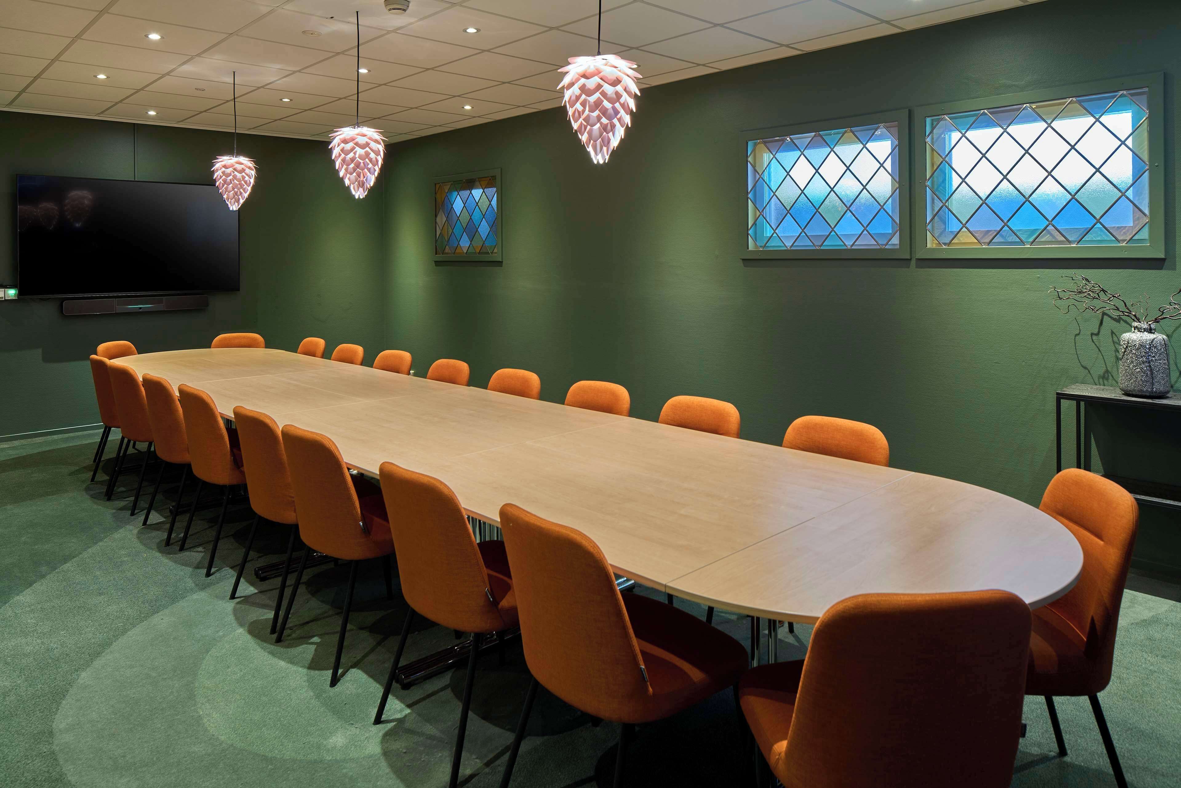 A conference room with a long table, orange chairs, a flat-screen TV, and decorative hanging lights.