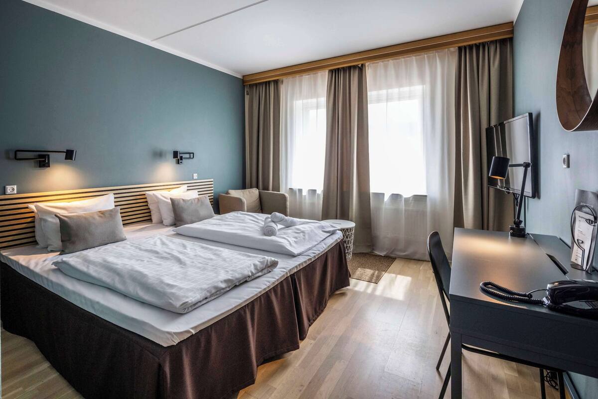 A hotel room with two beds, a desk, a chair, a telephone, and a TV.
