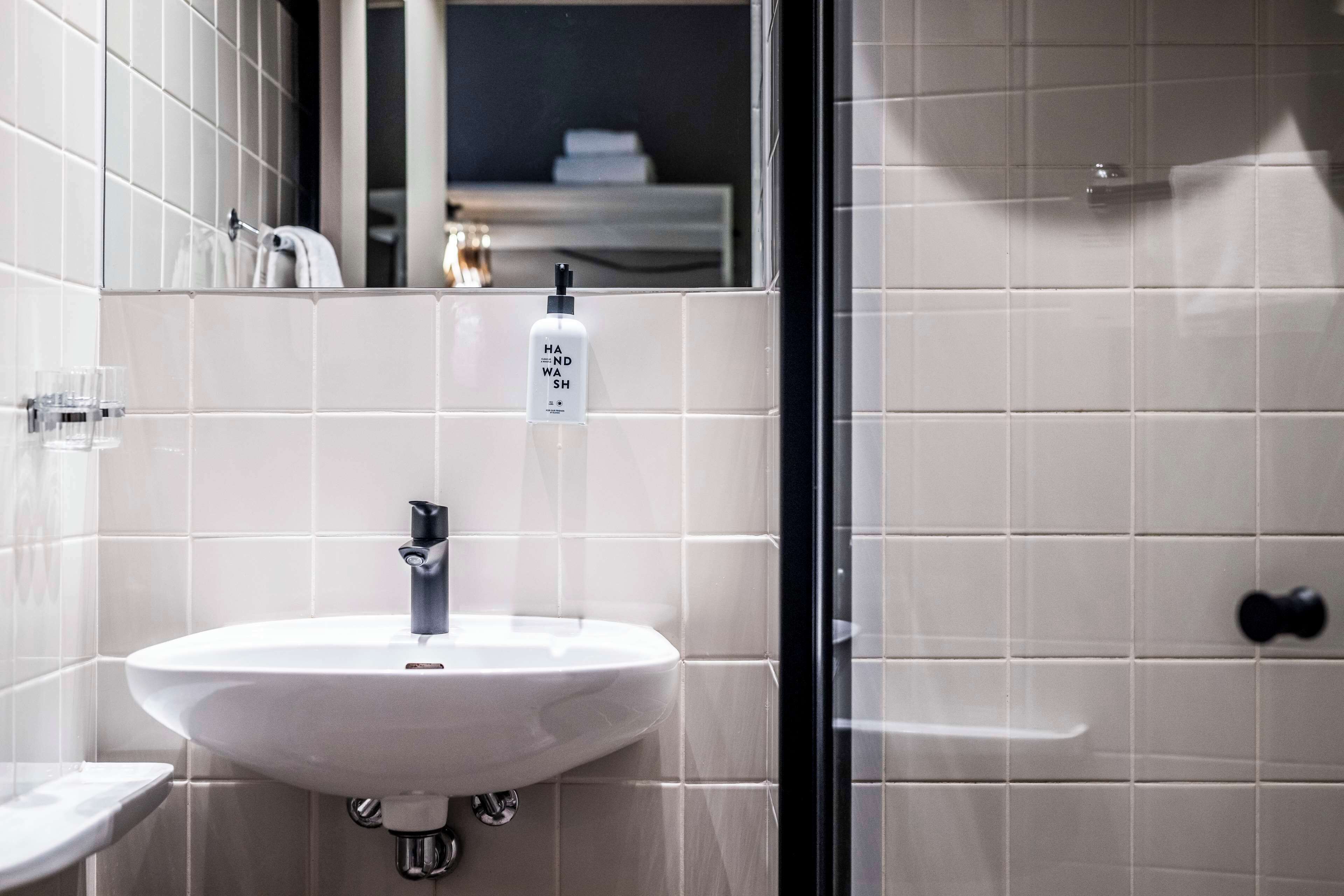 A bathroom with a white sink, a mirror, and a bottle of hand wash soap.