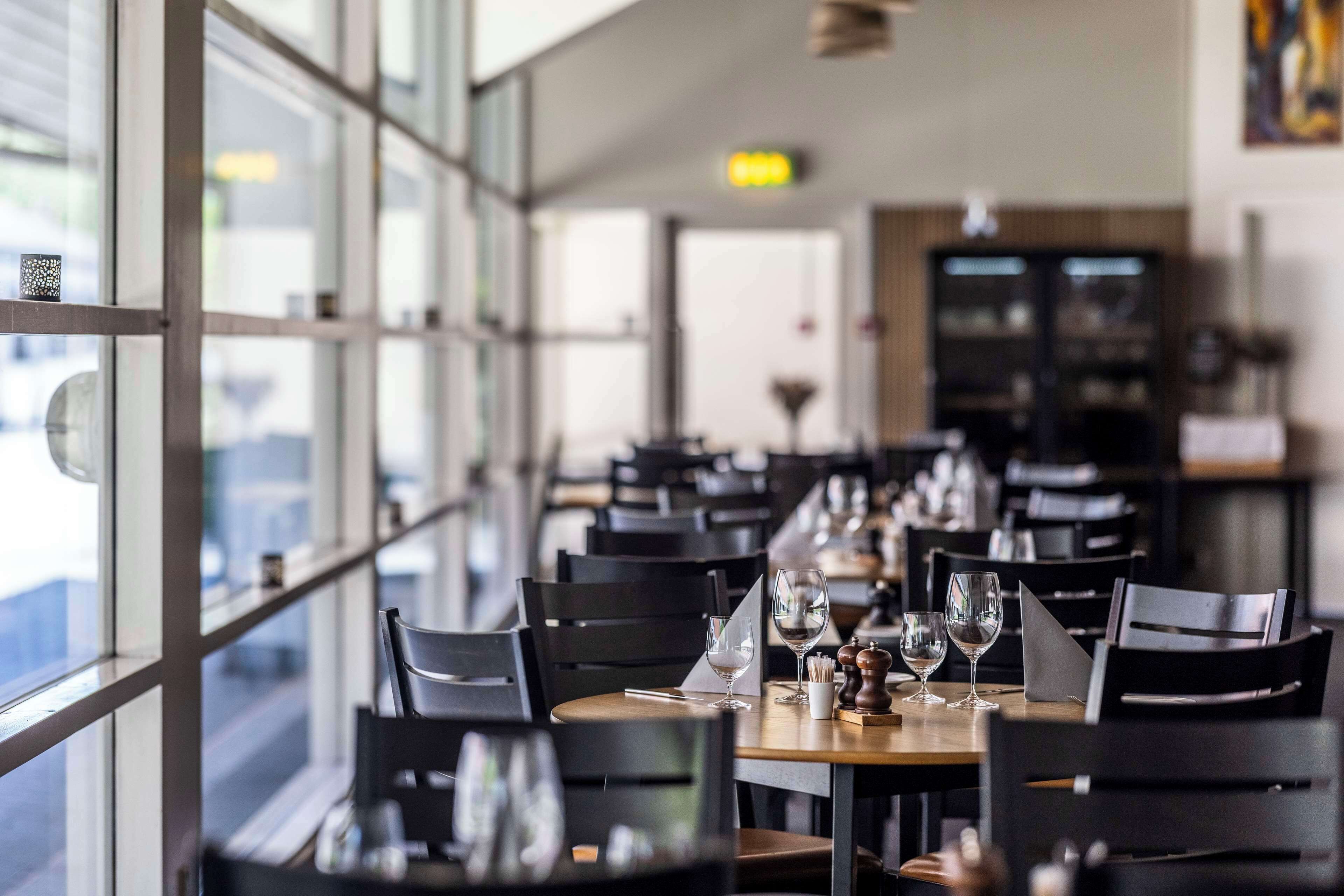 Un restaurante con una larga mesa dispuesta para comer, amplias ventanas y una decoración interior moderna.