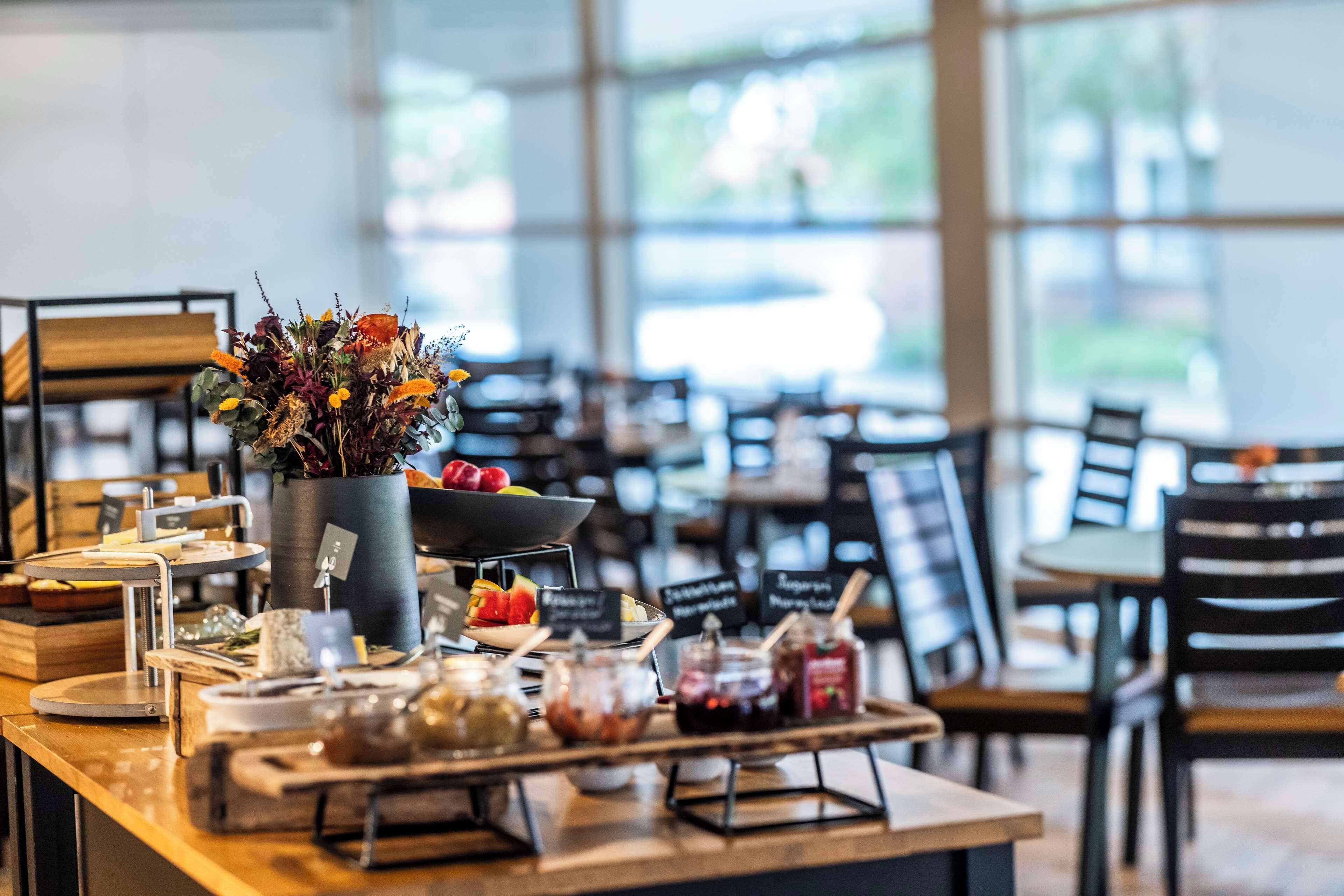 Mostrador de restaurante con diversos alimentos y condimentos, un jarrón de flores y pizarras con artículos del menú.