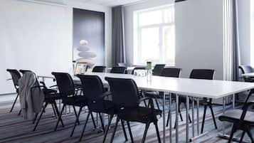 A conference room with a long table, black chairs, a whiteboard, and a window with curtains.