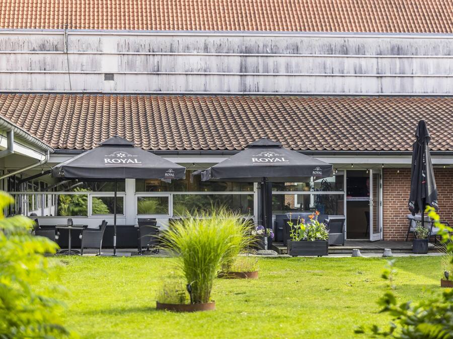 A restaurant with outdoor seating, covered by umbrellas, and a brick building with a tiled roof.