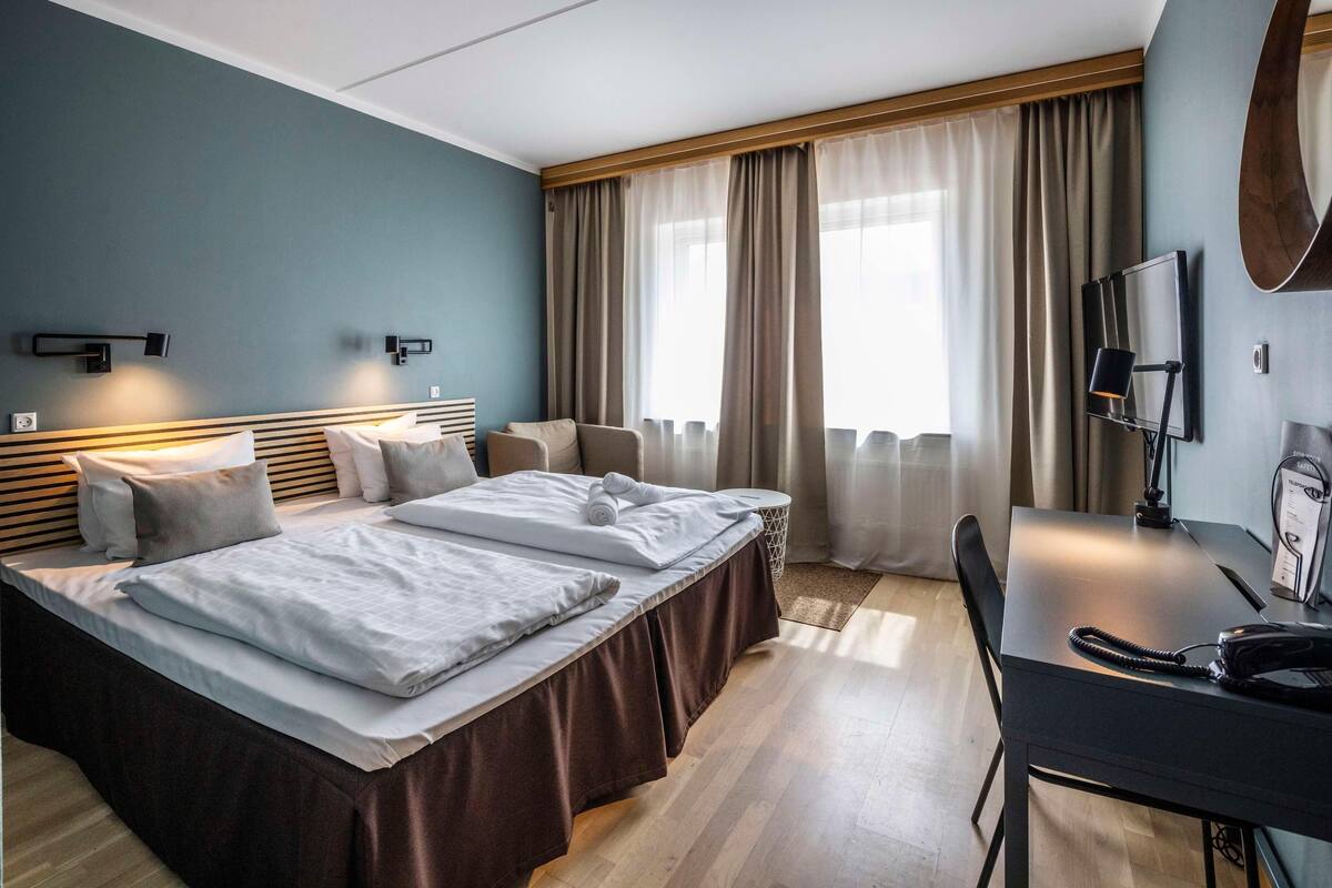 A hotel room with two beds, a desk, a chair, a telephone, and a TV.