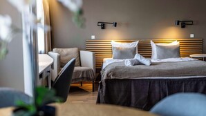 Una habitación de hotel moderna con cama, escritorio y silla. Hay luces empotradas sobre la cama y una pequeña mesa redonda a su lado.