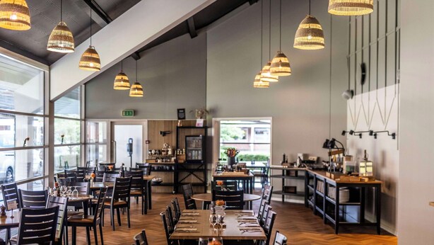 Un restaurante espacioso con techos altos, candelabros de mimbre colgantes y una zona central de comedor con mesas y sillas.