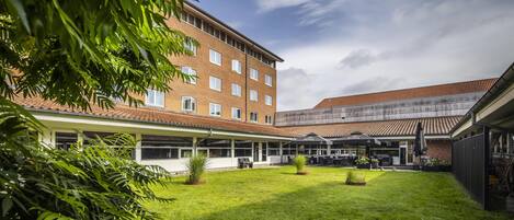 A hotel courtyard with a green lawn, outdoor seating, and a brick building with multiple windows.