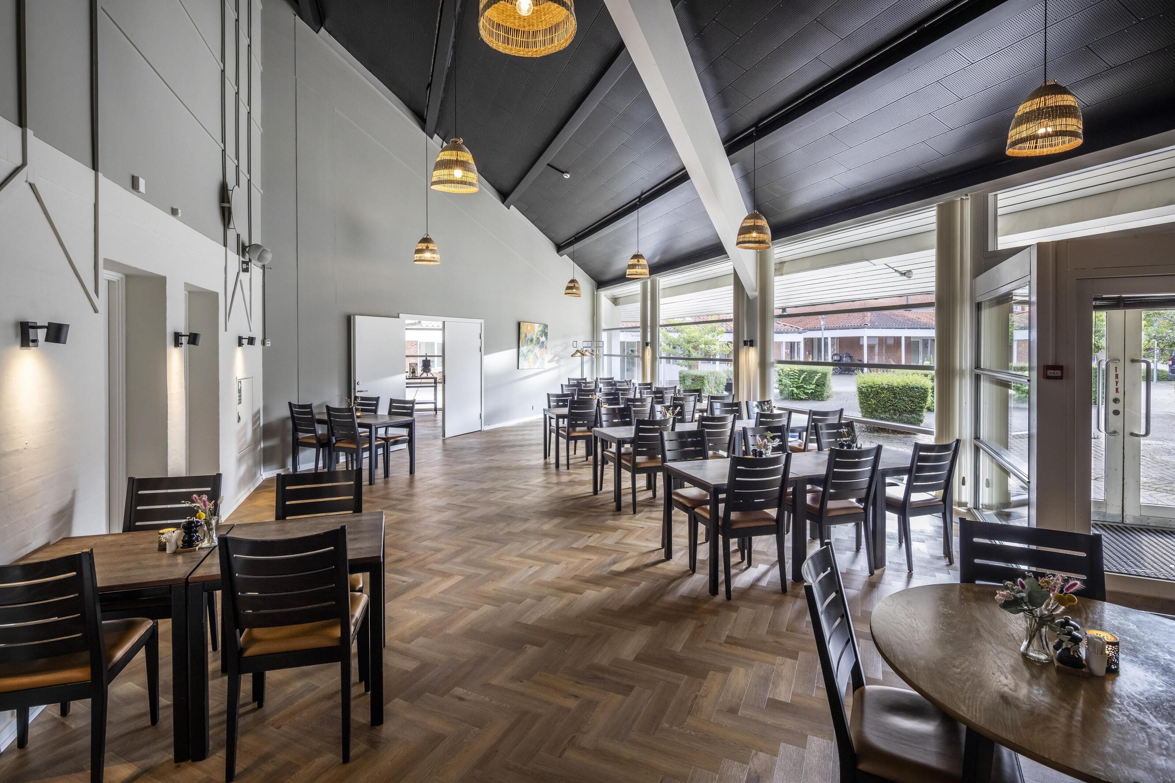 Un vaste espace dédié à la salle à manger, avec de nombreuses tables et chaises, de grandes fenêtres et des luminaires suspendus.