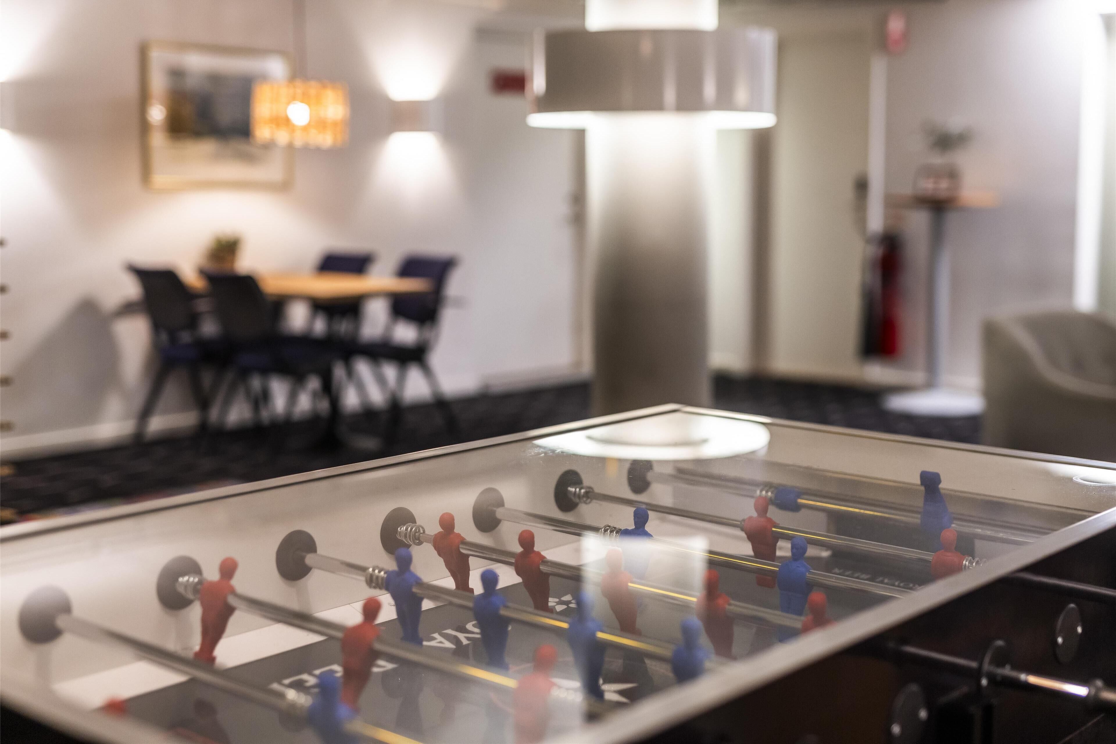Una mesa de futbolín en una habitación de hotel, con una zona de comedor al fondo.