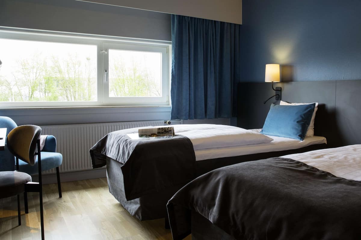 Una habitación de hotel con dos camas, una ventana con cortinas, una silla y una lámpara.