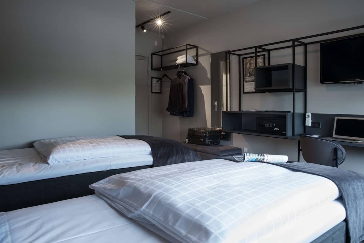 Habitación de hotel con dos camas, un escritorio, televisor y armario.